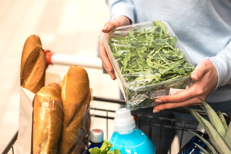 Beautiful young woman choosing green leafy vegetables in grocery store. Healthy food shopping concept.の写真素材