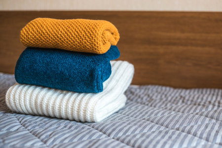 Pile of cozy knitted sweaters on bed. Autumn-winter conceptの写真素材