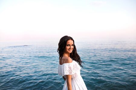 Young beautiful woman standing in white dress on the rock in the sea.の写真素材