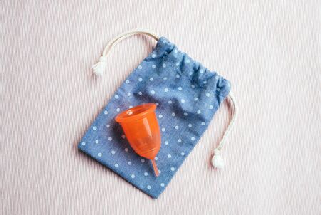 Orange menstrual cup on blue cotton bag on pink background. Womans health and environmentally friendly feminine hygiene product concept.の写真素材