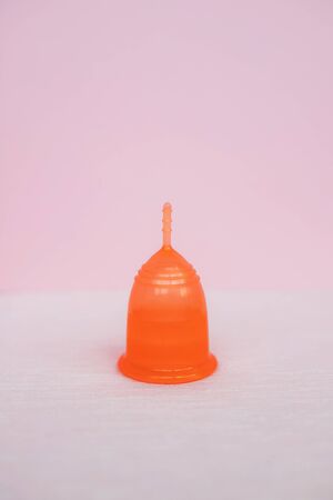 Orange menstrual cup on a light pink background. Close up.の写真素材