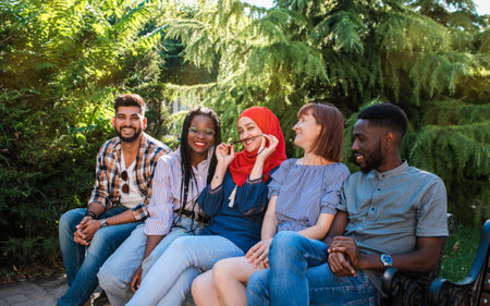 Multiracial young friends sitting by the street laughing and having fun together.