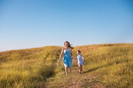 Young mother and daughter running in a golden field of sunshine while on a summer holiday. Family activities and outdoors concept.の写真素材