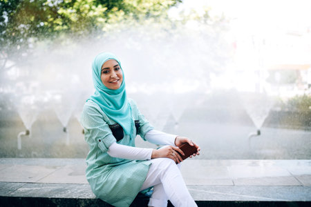 Beautiful young muslim woman using smartphone outdoor. Woman wearing hijab using mobile phone on the...