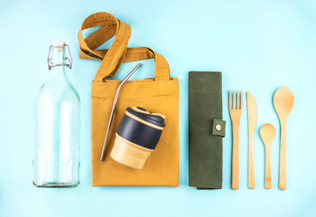 Eco bags with bamboo cutlery, reusable coffee mug and water bottle on blue background. Sustainable...