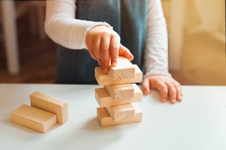 Little girl playing with wooden bricks at home. She builds little tower.の写真素材