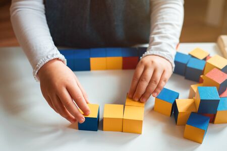 Little girl playing with colorful wooden bricks at home. She builds little house.の写真素材
