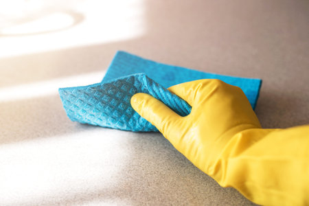 Womans hand in yellow glove with sponge cleaning the table.