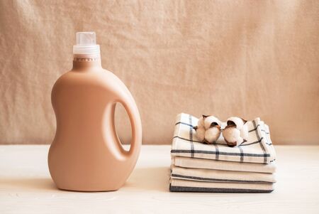 Gel for laundry washing in plastic bottle near a pile of fresh towels. Composition on white wooden shelf against textile background.の写真素材
