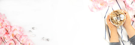 Easter banner with childs hands holding Easter eggs on wooden background. Pink spring flowers on...