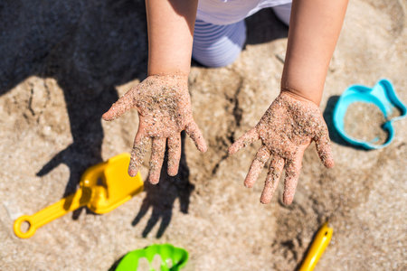 Close up hands of happy girl playing in sand on the beach.