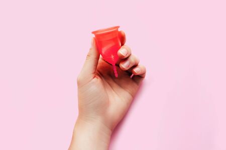 Womans hand holding menstrual cup over pink background. Womans health and environmentally friendly feminine hygiene product concept.の写真素材