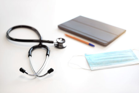 Doctors table at medical clinic. Stethoscope, mask and digital tablet are on the table.