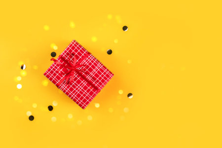 Red gift box on yellow background with golden confetti and rolls.