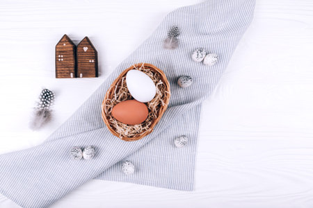 Easter eggs in the nest on textile napkin on white wooden background.