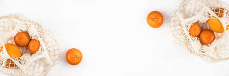 Banner made from mandarins and orange in a mesh bag on white wooden background. Flat lay. Zero waste.の写真素材