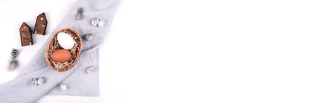 Banner made from Easter eggs in the nest on textile napkin on white wooden background.