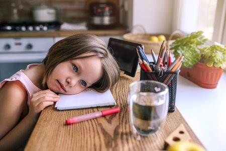 Tired girl sitting at a table with a digital tablet after an online lesson.