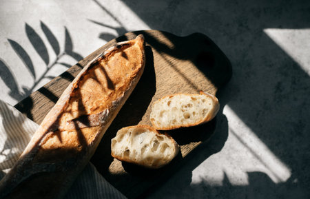 French fresh bread baguette with slices on a ceramic plate on gray background.