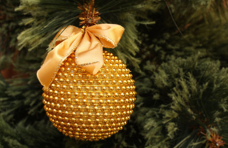 A gold glitter Christmas ball hanging in a decorated tree.
