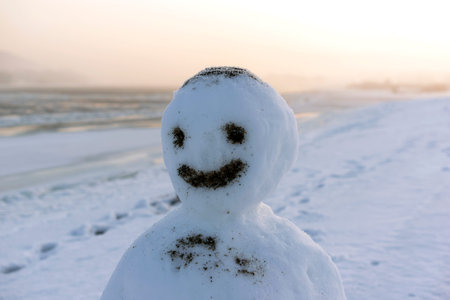 Happy face snowman standing near the river in cold winter morning.