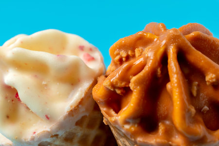 Two cone ice cream with caramel and white chocolate on blue background.