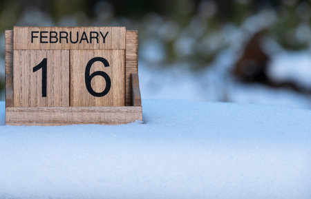 Wooden calendar of February 16 date standing in the snow outdoors in nature.の写真素材