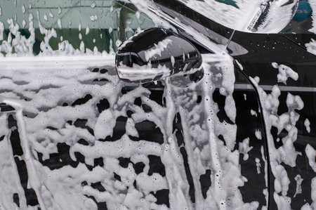 A detailed image showing a car covered in soapy foam during a wash. The bubbles and soap convey a sense of freshness and cleanliness, enhancing the vehicle's shiny surface.の写真素材