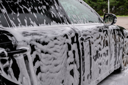 A detailed image showing a car covered in soapy foam during a wash. The bubbles and soap convey a sense of freshness and cleanliness, enhancing the vehicle's shiny surface.の写真素材