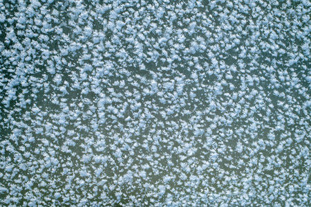 An aerial view of a water surface lightly dusted with snow crystals, creating a frosted pattern...