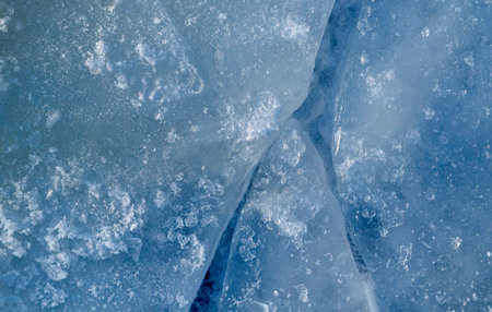 A detailed close-up of blue ice showing jagged cracks, crystalline snow, and glistening ice shards....