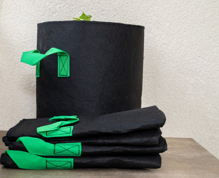 Black fabric grow bags with bright green handles and a small seedling, folded on a table next to an...
