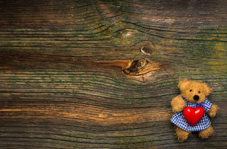 Teddy bear holding red heart on wooden background. Free space for your text.の写真素材
