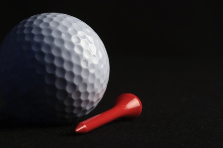 Golf ball with red tee on black background の写真素材