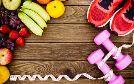 Fitness, healthy fruits, diet and active lifestyles Concept, dumbbells, tape measure, sport shoes, fresh fruits on wood background. copy space for text. Top viewの写真素材
