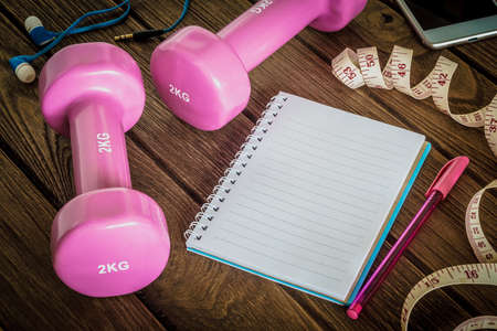 Fitness, healthy and active lifestyles Concept, dumbbells, blank notebook, measuring tape, smartphone with headphone on wood background. copy space for text. Top viewの写真素材