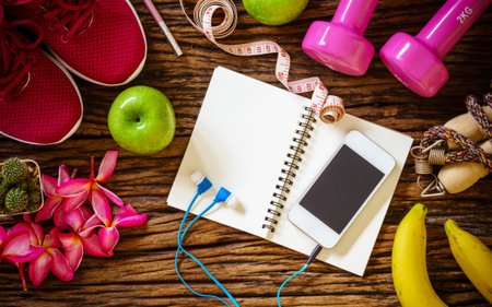 Still Life - Fitness, healthy and active lifestyles Concept, dumbbells, sport shoes, measuring tape, Jump rope, bananas, apples smart phone and headphone on wood background. Top view with copy space for text.の写真素材