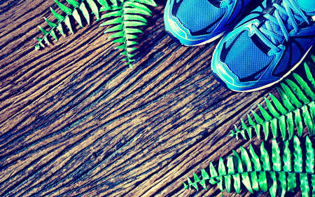 Pair of blue running shoes laid on a grunge wooden floor background with nature ferns, top view with copy spaceの写真素材