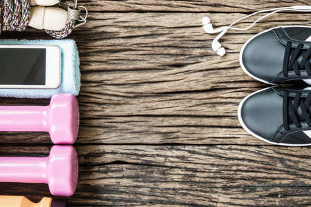 Fitness, healthy and active lifestyles Concept, dumbbells, sport shoes, bottle of waters, smartphone with headphone, banana and apples on wood background. copy space for text. Top viewの写真素材