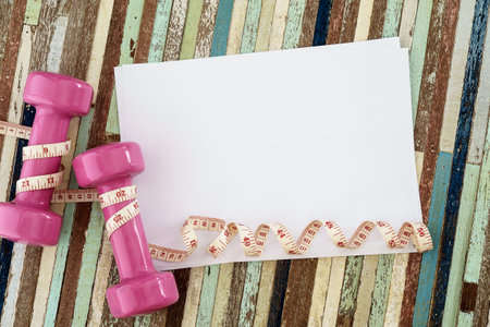 pink dumbbell and measuring tape and blank paper for your text on wooden background,Sport...
