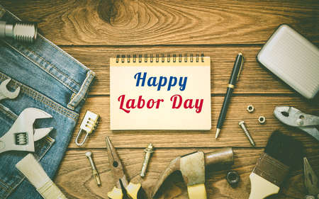 Labor day background concept - Jeans, many handy tools, notebook with happy labor day text on wooden background top viewの写真素材