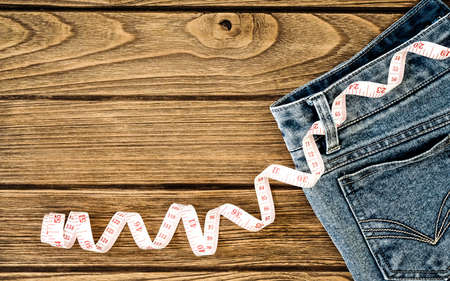 Weight loss concept, Blue jeans and measuring tape on wooden background, Top view with copy spaceの写真素材