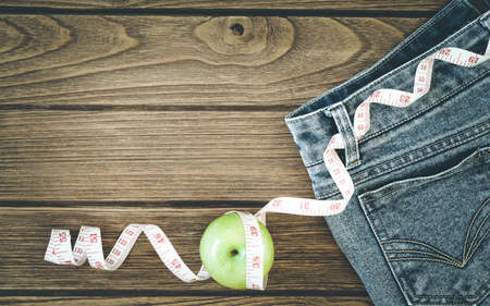 Weight loss concept, Blue jeans, green apples and measuring tape on wooden background, Top view with copy spaceの写真素材