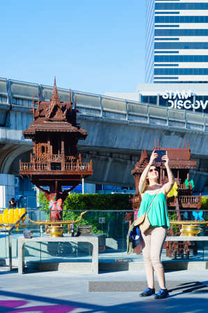 BANGKOK, Thailand - APRIL 12, 2017:  Unidentified tourist are taking selfie in front of the Thai outdoor spirit house shrine on the BTS skywalk near MBK Shopping centerのeditorial素材