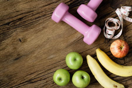 Fitness, healthy and active lifestyles Concept, dumbbells, measuring tape, bananas and apples on wood background. Top view with copy space.の写真素材