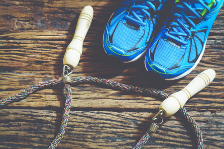 Fitness, healthy and active lifestyles, red sport shoes and jump rope on wooden  background