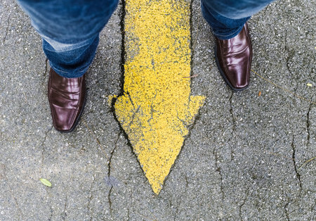 Man wear brown leather shoes standing over arrow sign at footpathの写真素材