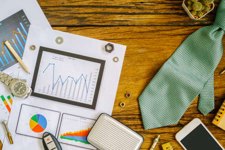 labor and fathers day background concept, financial charts and graphs, smartphone, necktie, watch, car key on the table, top viewの写真素材