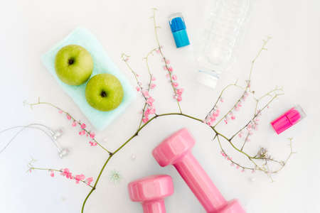 Fitness, healthy and beauty lifestyle concept, dumbbells, cosmetics, green apples, earphones, bottle of water and flowers on white backgroundの写真素材