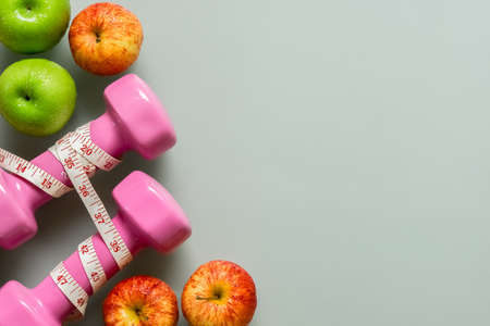 Dieting, healthy and active lifestyles Concept, apples, tape measure  and dumbbells on grey background. top view with blank copy spaceの写真素材